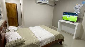 A bedroom with a bed, a television on a stand, an air conditioning unit, and a door.