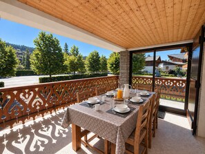 A dining area with a table set for four, a wooden ceiling, and a view of a residential area with trees and houses. - Peaceful family chalet - 6 guests (Les Gets)