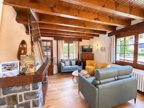 A cozy room with a stone fireplace, a sofa, a television, and a window with a view of greenery. - Peaceful family chalet - 6 guests (Les Gets)
