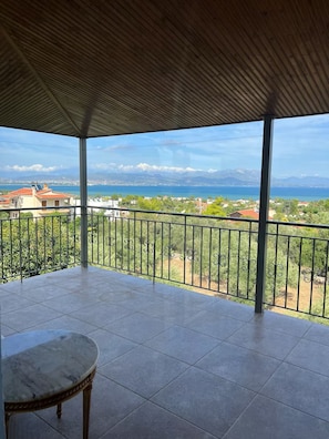 A covered balcony with a view of a coastal landscape, a tiled floor, and a single chair. - The sea view house of Xenia and Panos by MPS (Paralia Avlidos)