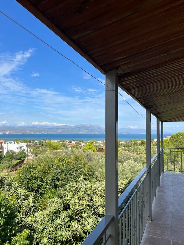 Uma varanda com vista para a paisagem costeira, incluindo um corpo d'água e montanhas ao longe.