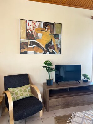 Ein Wohnzimmer mit einer Couch, einem Fernseher auf einem Holzgestell und einem Bild an der Wand.