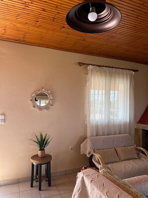 Um quarto aconchegante com uma cama, uma mesinha com uma planta, um espelho e uma janela com cortinas.