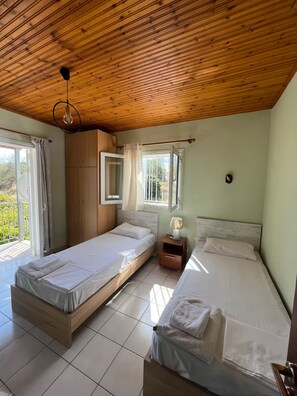 Quarto com duas camas, teto de madeira, janela com cortinas e mesa de cabeceira com abajur.