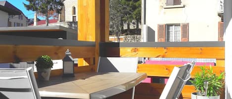 An outdoor seating area with a table and chairs, surrounded by a wooden fence, overlooking a residential street with houses and trees.