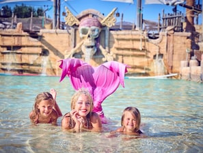 Ein Wasserpark mit einem Meerjungfrauen-Schwanz, Felsformationen und einem klaren, blauen Pool.