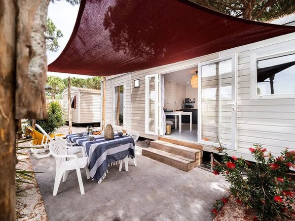 Une maison mobile dotée d’un patio, d’une table à manger et d’une cuisine visible à travers la porte ouverte.
