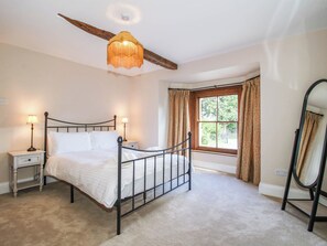 A bedroom with a bed, bedside tables, a mirror, a window with curtains, and a hanging light fixture. - Stone House Farm (Leominster)