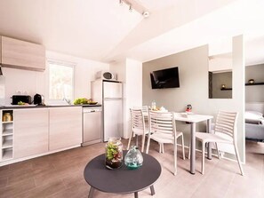 A modern kitchen with white cabinets, a refrigerator, and a dining area with a table and chairs. - Cozy mobile home, AC - 6 guests (Agde)