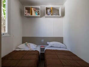 Une chambre avec deux lits, une fenêtre et des étagères intégrées où sont rangés des livres et des jouets.