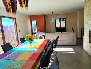 A dining area with a colorful tablecloth, a vase with flowers, and a view through the window. - Mountain lodge, Vosges view (Goldbach-Altenbach)