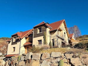 A multi-story house with a stone wall in the foreground, a red-tiled roof, and a clear blue sky. - Mountain lodge, Vosges view (Goldbach-Altenbach)