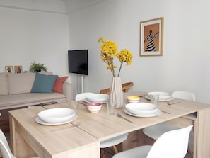 A dining area with a wooden table set for four, surrounded by white chairs. A flat-screen TV is mounted on the wall above the table. - Renovated apartment in historic center - 5 guests (Sevilla)