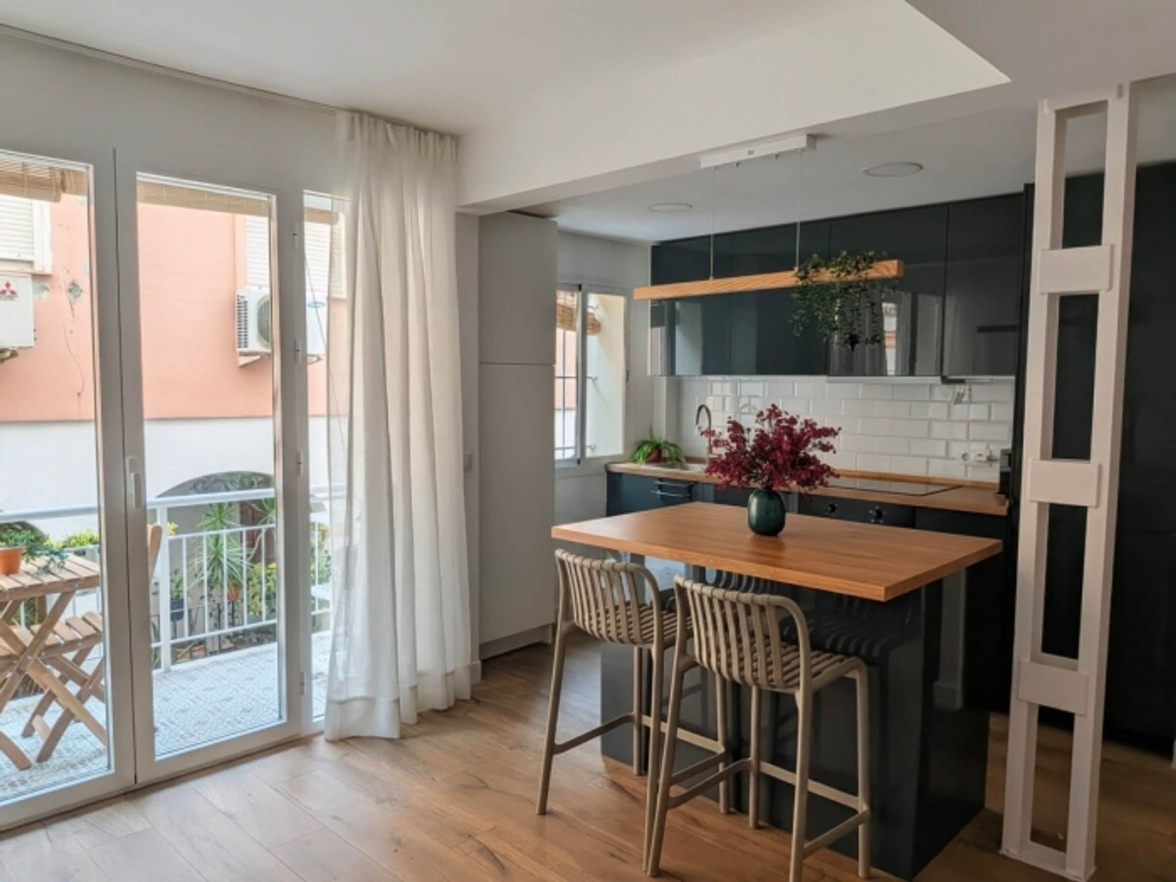 A modern kitchen with a wooden island, two bar stools, and a potted plant.