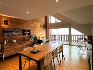 A modern kitchen with wooden cabinetry, a dining area with a wooden table and chairs, and a balcony with a view. - Spacious apartment, panoramic view - 10 guests (Villard-de-Lans)