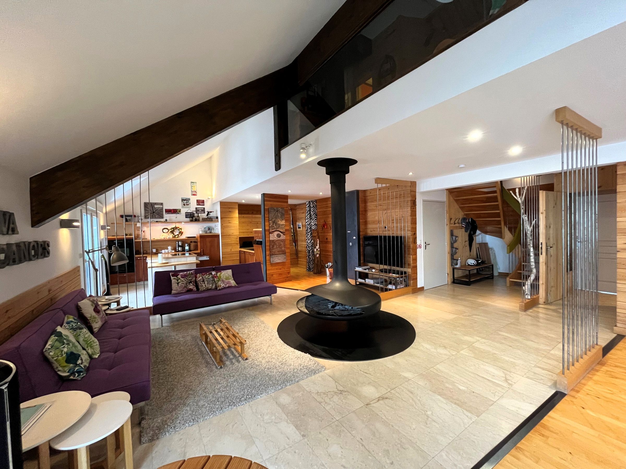 Een ruime woonkamer met een hoge plafond, een open haard, een paarse bank en een trap naar een verdieping.