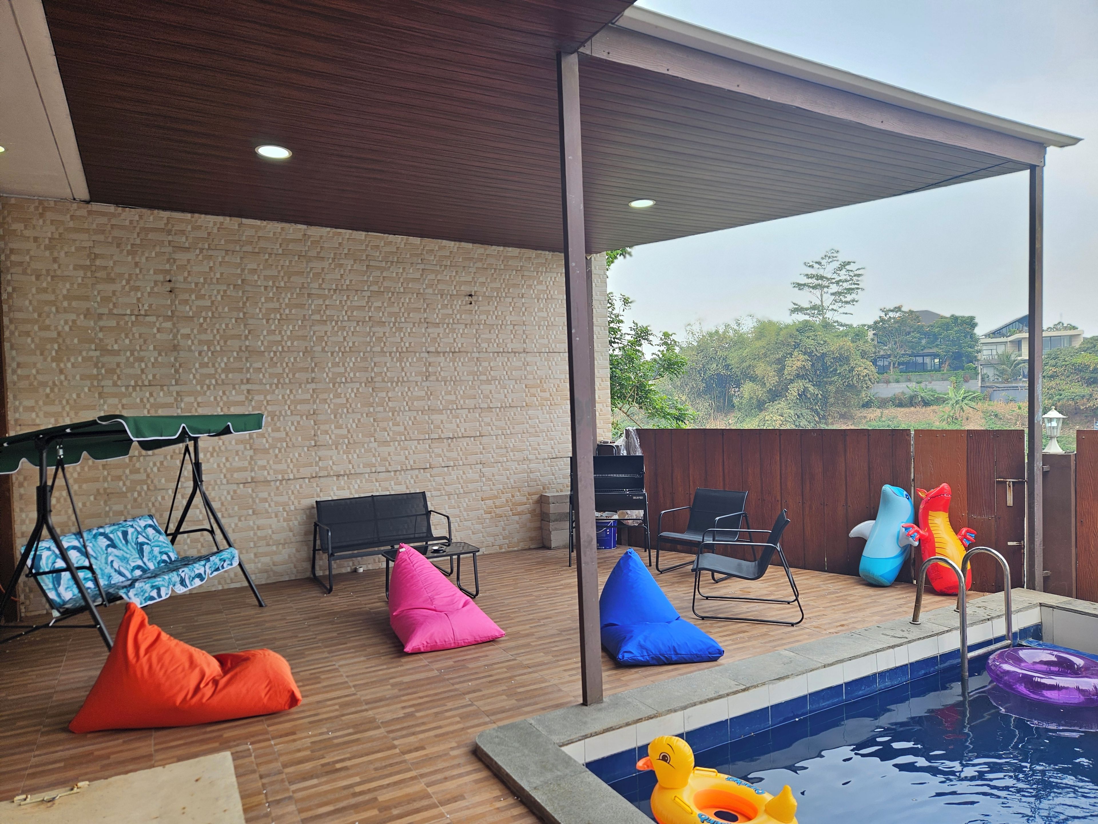 An outdoor pool area with a swing chair, bean bags, and inflatable toys.