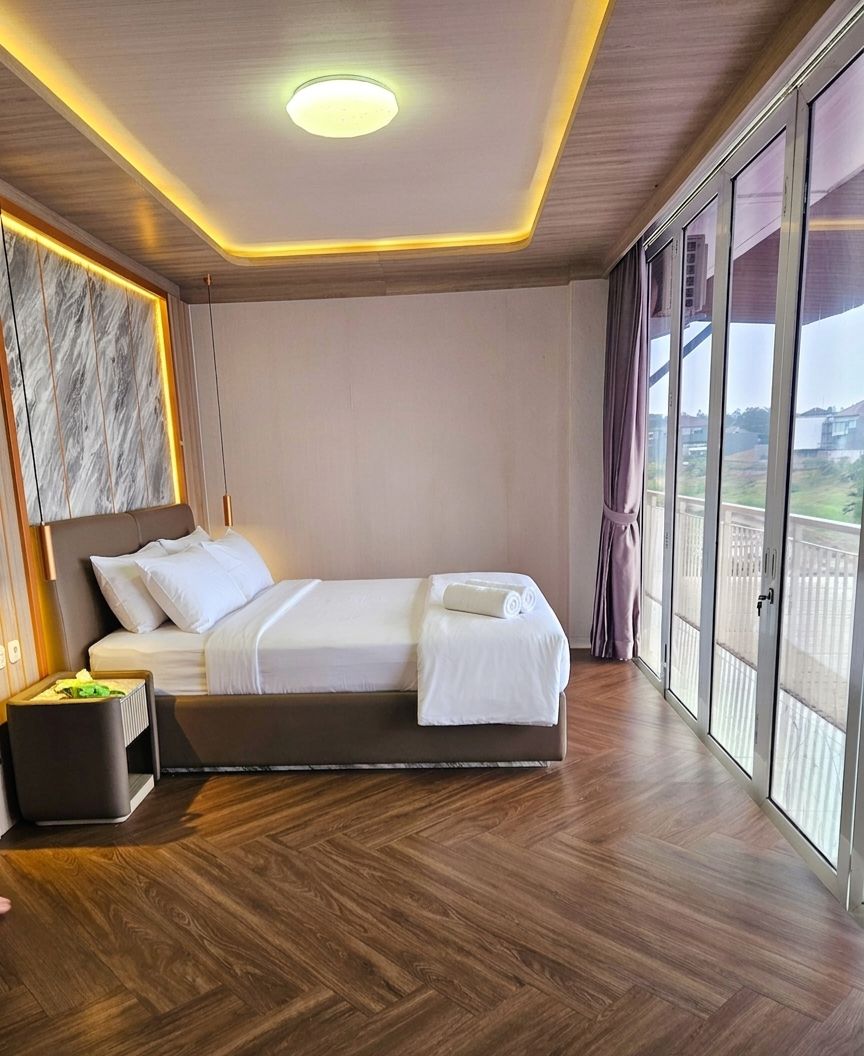Ein Hotelzimmer mit einem Bett, einem Nachttisch, einem Fenster mit Vorhängen und Blick nach draußen.