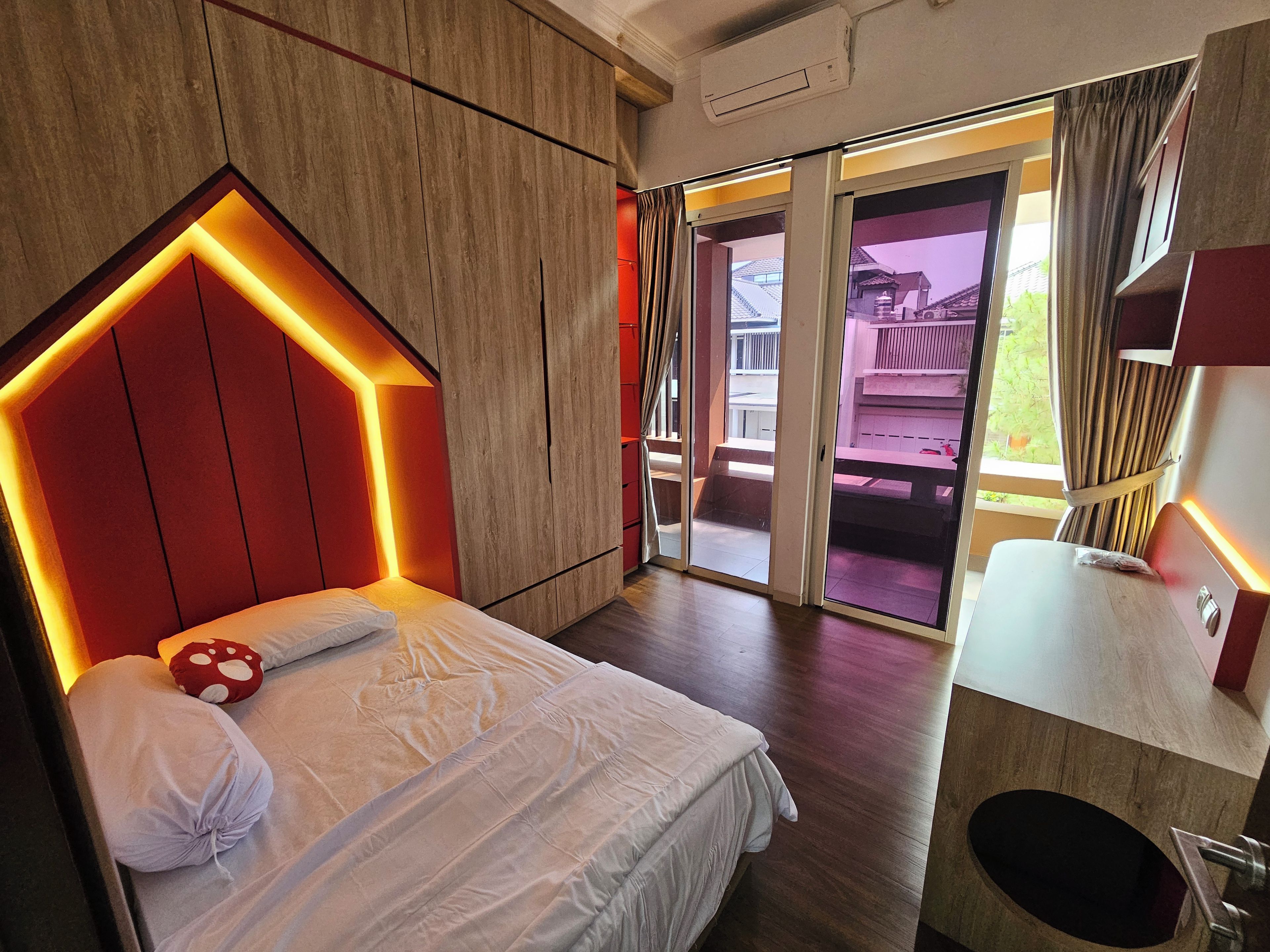 A hotel room with a bed, a wooden headboard, a bathroom, and a view of the outside.