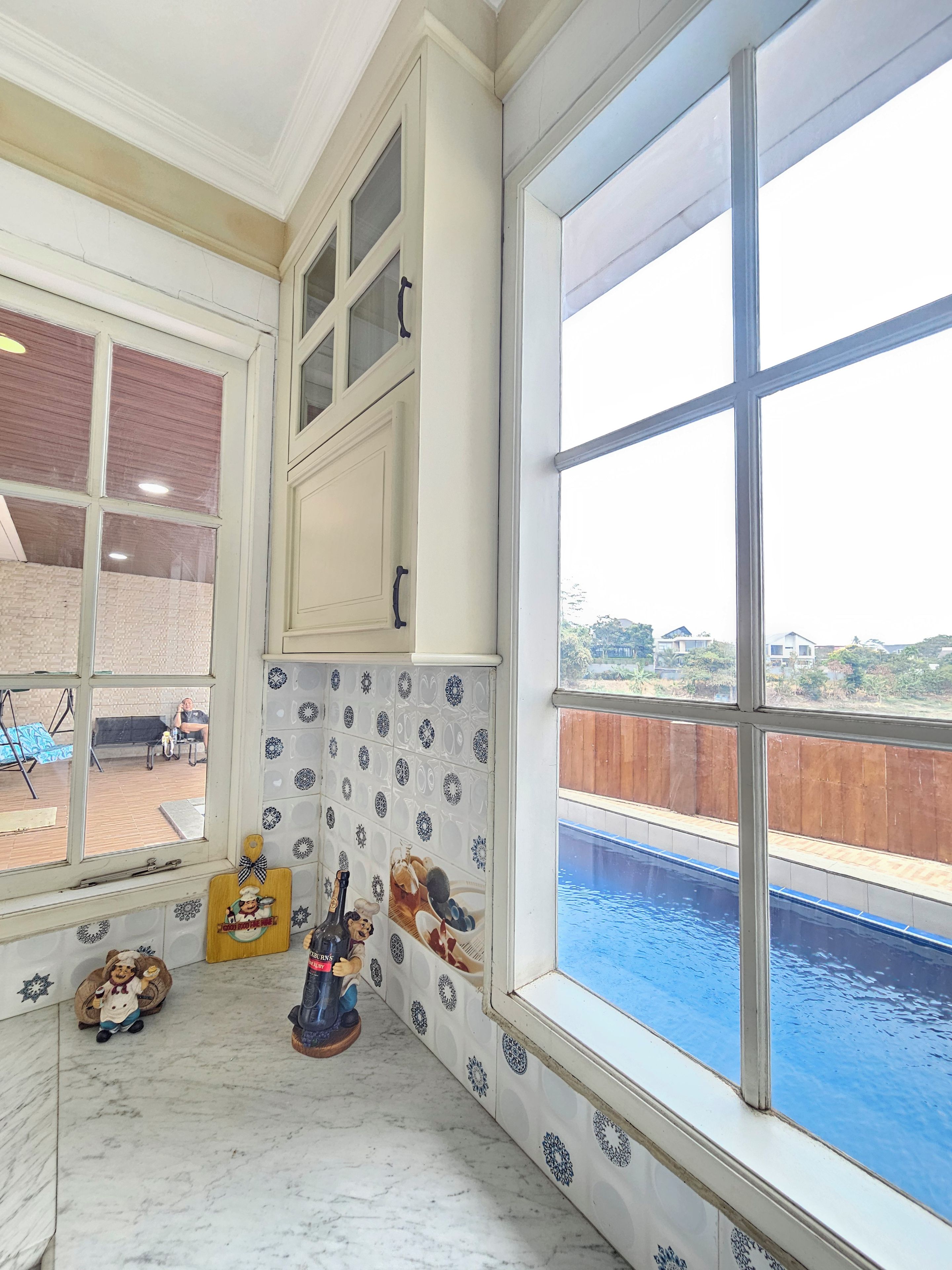 Eine Küche mit einem großen Fenster, einer gefliesten Spritzschutzwand und Blick auf einen Swimmingpool.