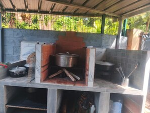 Ein Außenbereich mit Kochgelegenheit, einem Backofen aus Ziegeln sowie Töpfen und Kochutensilien.
