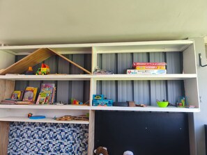 Ein Zimmer mit Fliesenboden, einer Tafel und Regalen mit Kinderspielzeug und Büchern.