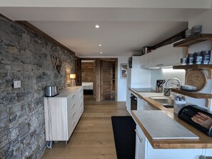 A modern kitchen with a stone wall, wooden cabinets, and a countertop with a bread machine. - Apartment with panoramic view - 4 guests (Cleurie)