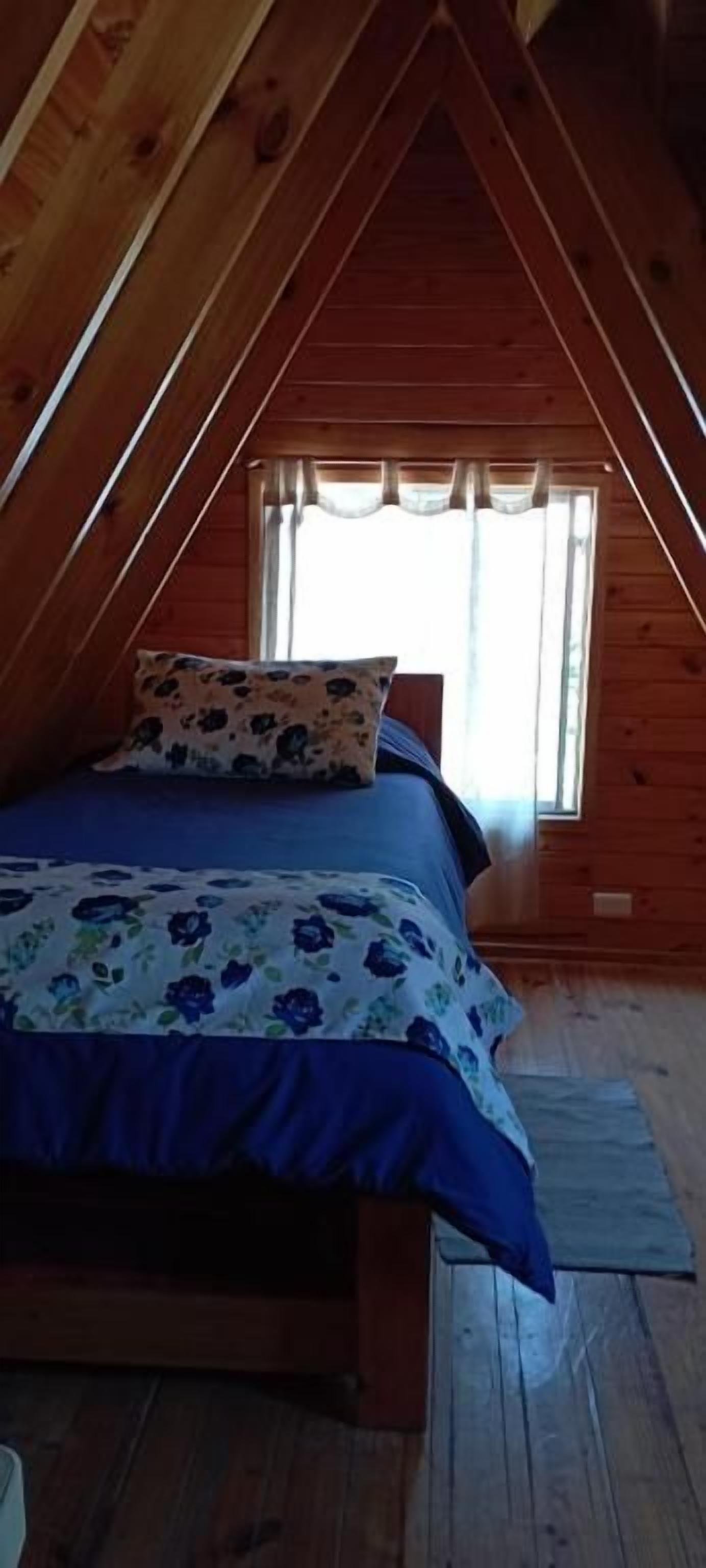 Un dormitorio con techo de madera, una cama con colcha estampada y una ventana con cortinas.