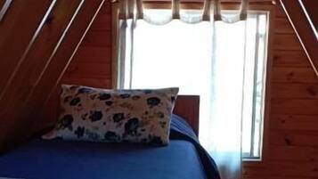 Un dormitorio con techo de madera, una cama con colcha estampada y una ventana con cortinas.