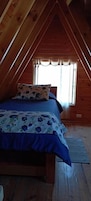 Un dormitorio con techo de madera, una cama con colcha estampada y una ventana con cortinas.
