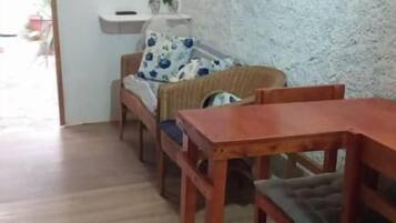 Una habitación con una mesa de comedor de madera, un sofá con un cojín floral y un televisor montado en la pared.