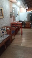 Un espacio habitable con un sofá, una mesa de comedor de madera y sillas. Se ve una cocina con refrigerador y estufa al fondo.