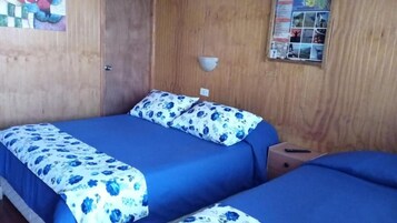 Una habitación con dos camas, una pared de madera, una lámpara de pared y un tablón de anuncios.