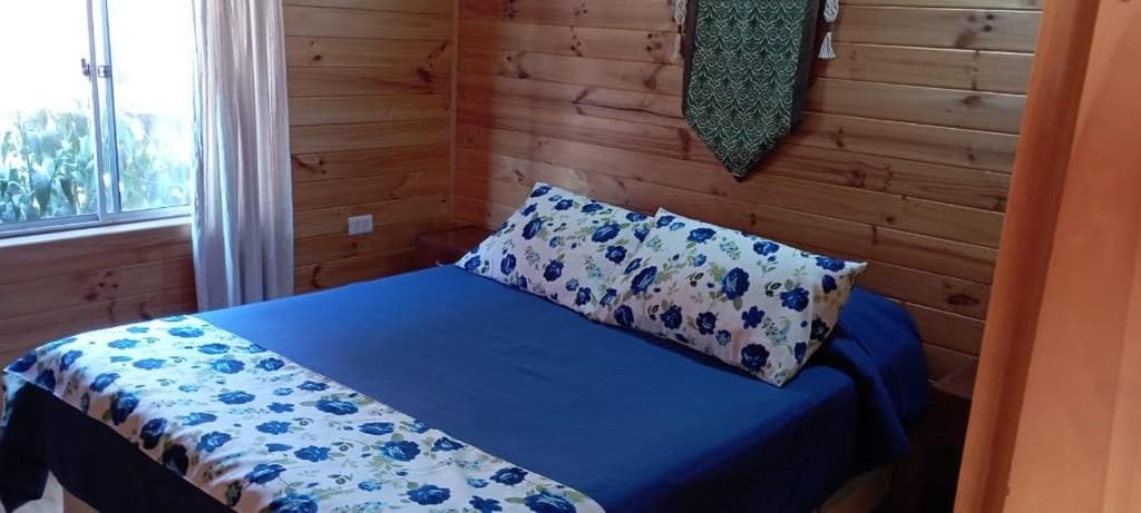 Una habitación tipo cabaña de madera con una cama, una ventana y una cortina.