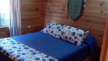 Una habitación tipo cabaña de madera con una cama, una ventana y una cortina.