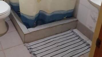 Un baño con cortina de ducha, inodoro, lavamanos y un estante pequeño.