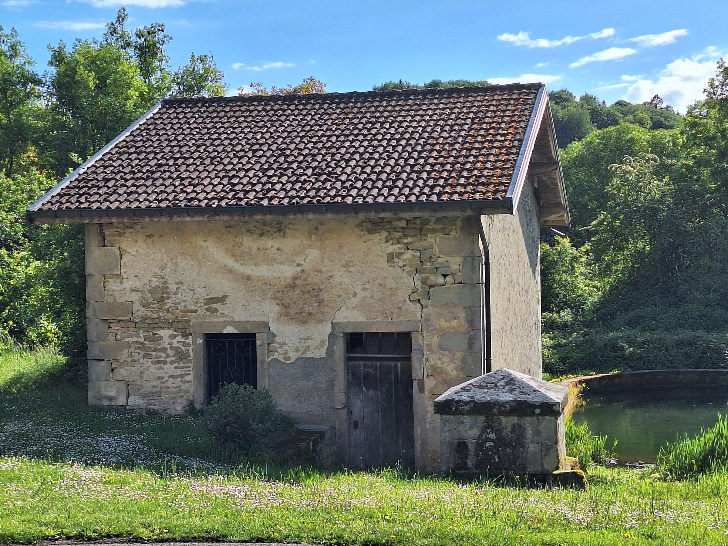 Un bâtiment rustique en pierre, avec un toit en tuiles, deux petites fenêtres et une seule porte.