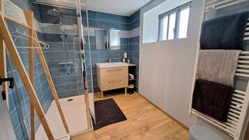 A modern bathroom with a glass shower enclosure, a wooden bench, a sink with a mirror, and a towel rack with multiple towels.