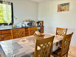 Une cuisine équipée d’un four à micro-ondes, d’un grille-pain et d’un évier. On y trouve une table à manger avec des chaises et un panier de pain.