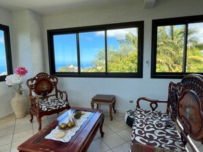 A room with two wooden chairs, a small table with decorative items, and a view of palm trees through large windows. - 3-Bedroom Air-conditioned Apartment near the Beach (Petite Île)