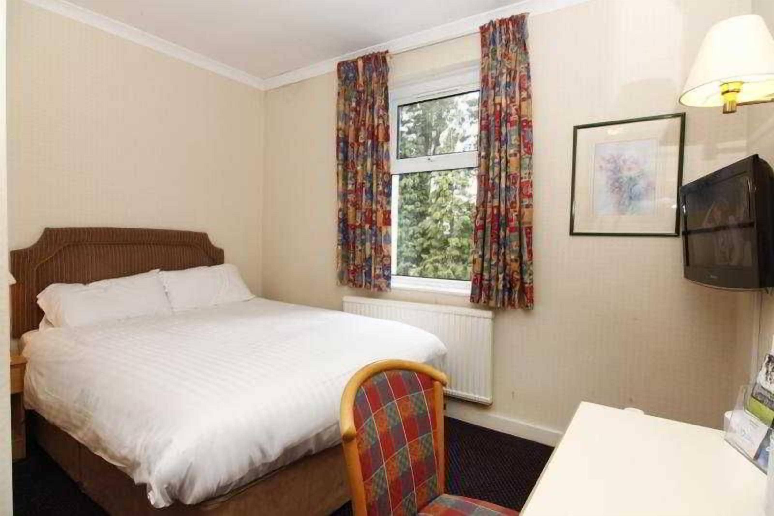 A hotel room with a bed, a desk, a chair, a television, and curtains.