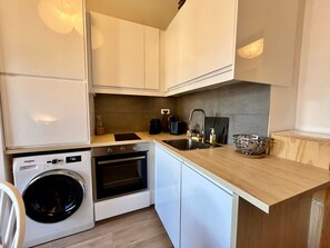 A compact kitchen with a built-in washer, oven, and a sink with a cutting board and basket. - Charming apartment center Morillon - 4 guests (Morillon Village)