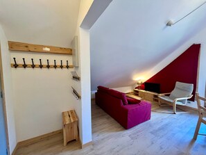 A cozy loft bedroom with a red accent wall, a wooden bench, a red sofa, a white chair, and a TV on a wooden stand. - Charming apartment center Morillon - 4 guests (Morillon Village)