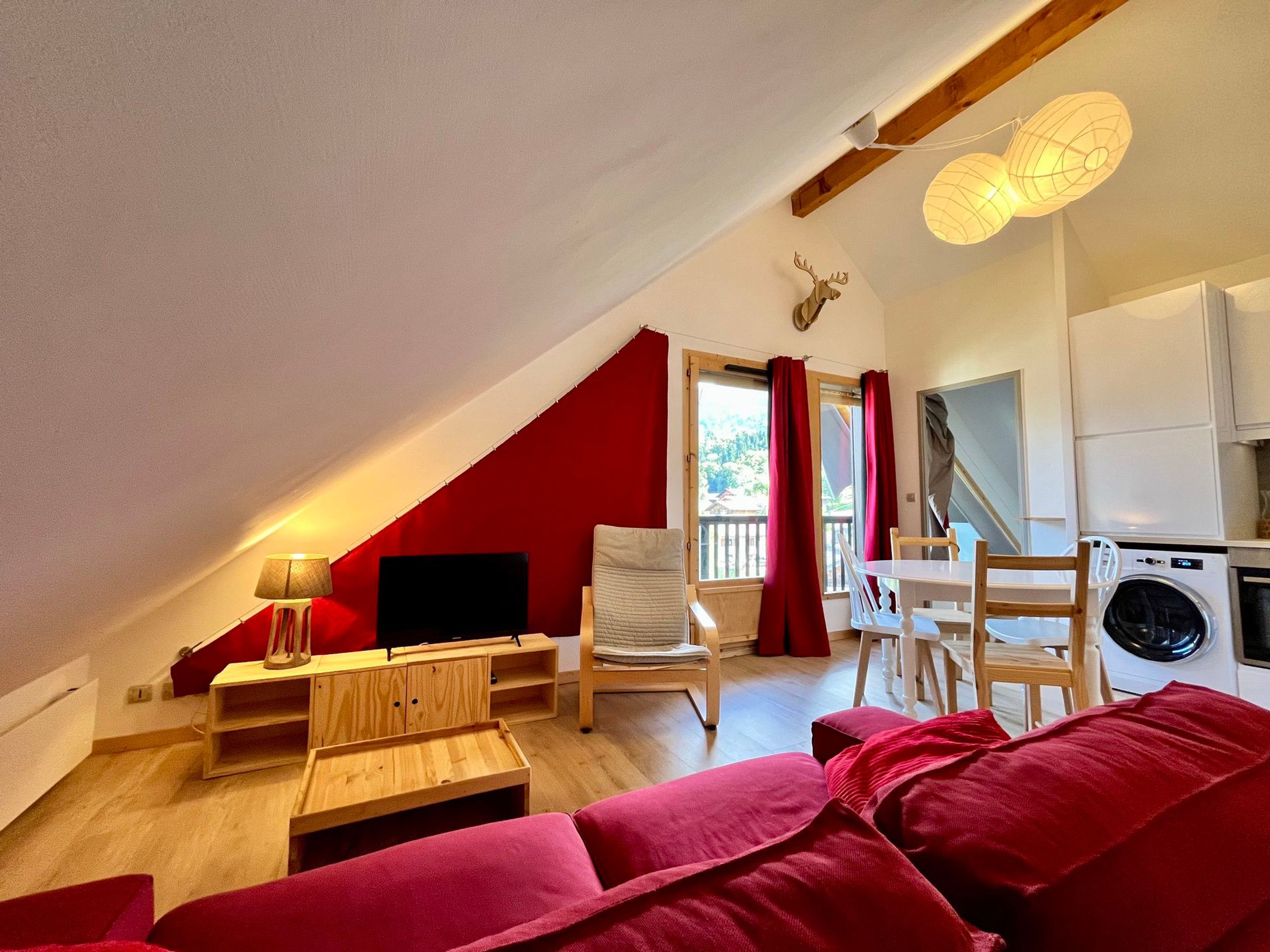 A cozy living room with a red accent wall, a wooden table, a sofa, a TV, and a ceiling fan.