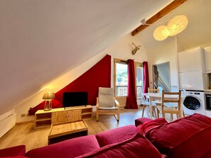 Un salon chaleureux avec un mur d’accent rouge, une table en bois, un canapé, un téléviseur et un ventilateur de plafond.