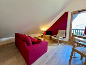 A red sofa, a wooden chair, a TV, and a balcony with a view. - Charming apartment center Morillon - 4 guests (Morillon Village)