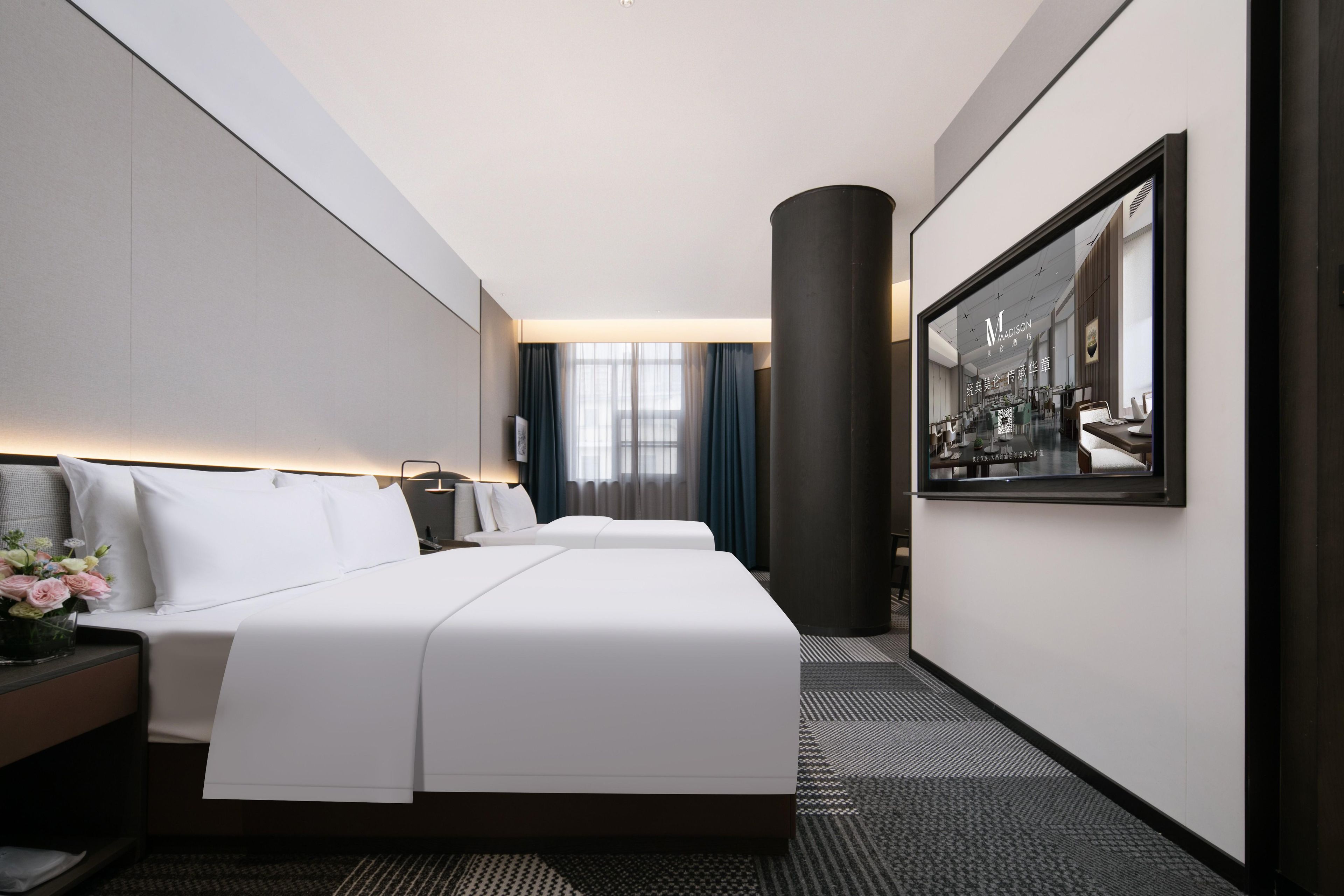Quarto de hotel com uma cama grande, mesa de cabeceira, escrivaninha e uma janela ampla com cortinas.