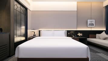 A modern hotel room with a large bed, a desk, a chair, and a nightstand.