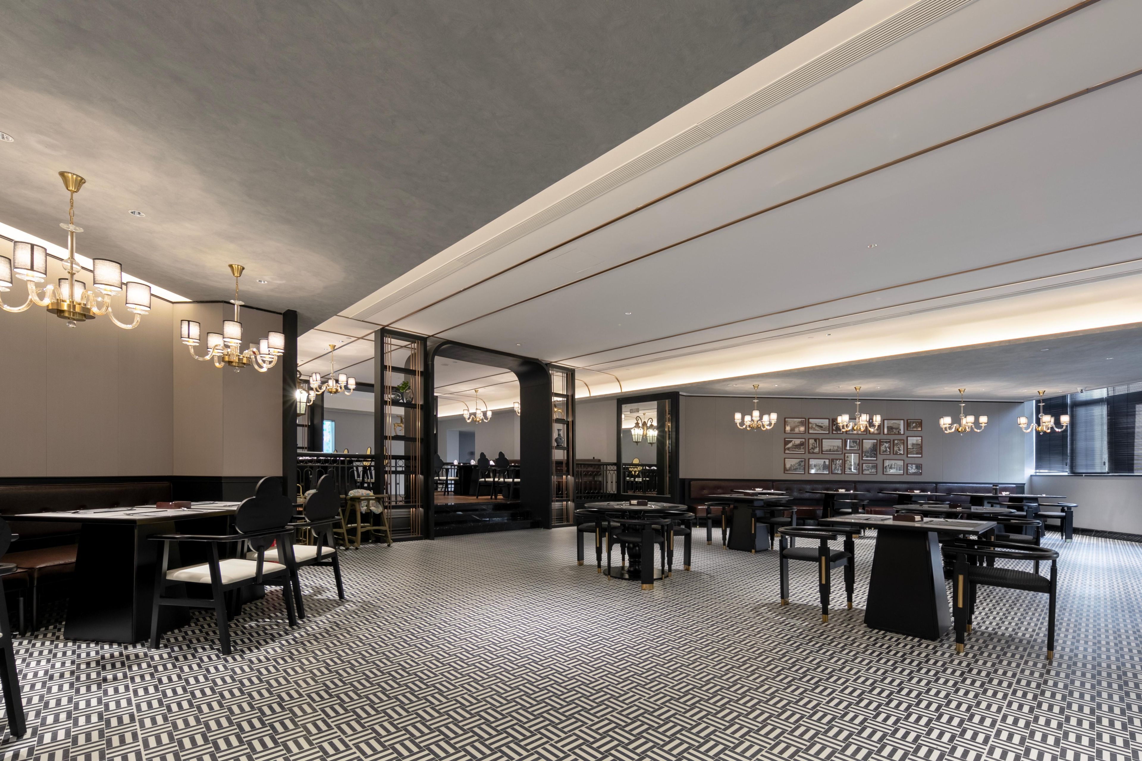 Um restaurante moderno com piso em padrão preto e branco, várias mesas de jantar e lustres.