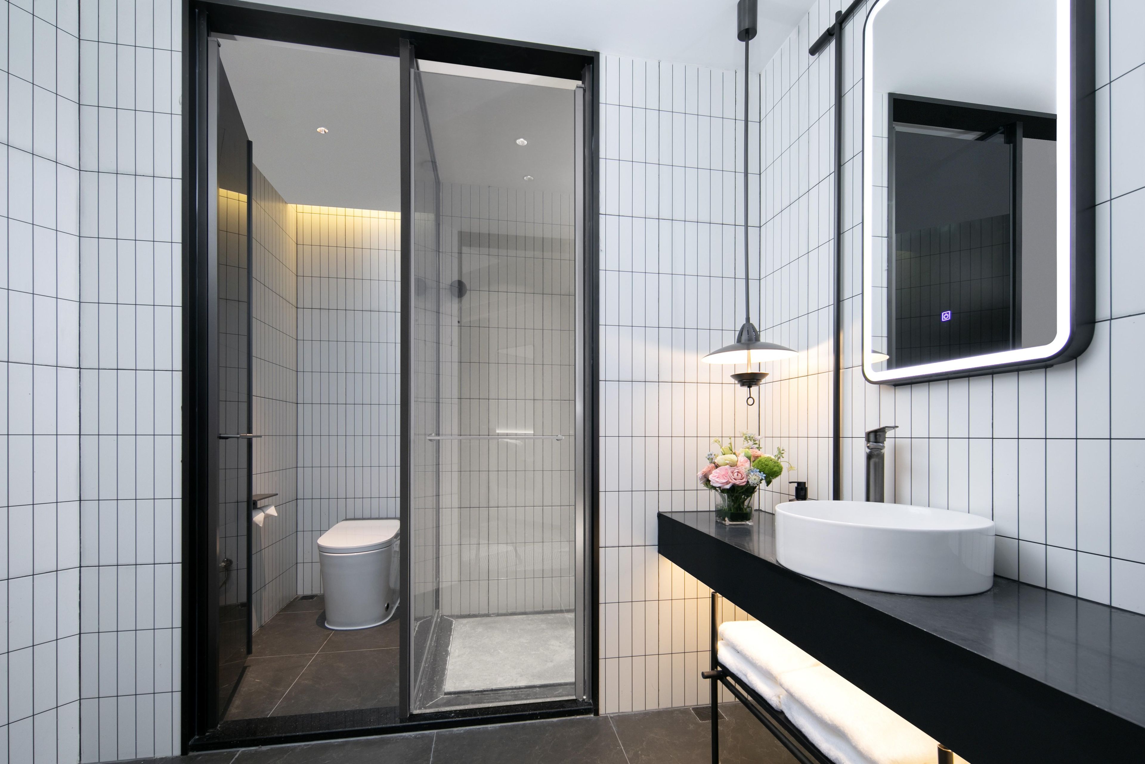 A modern bathroom with a glass-enclosed shower, a white toilet, a black countertop, a white sink, and a mirror.